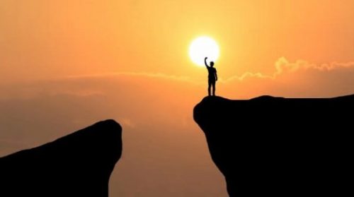 Person på bjergtop foran sol