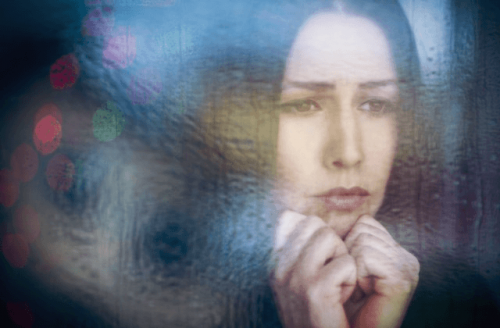 Kvinde, der kigger trist ud af vinduet, lider af dystymi