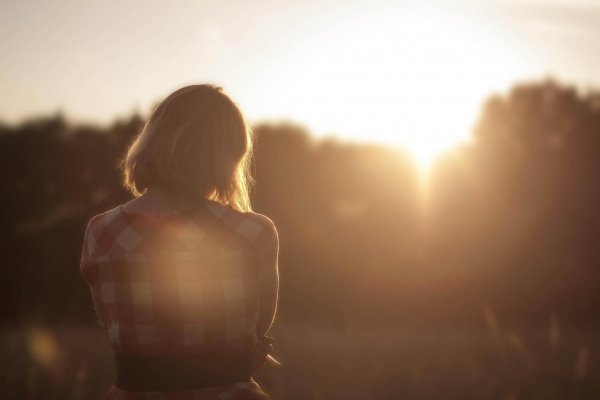 Kvinde står alene på mark og ser solnedgang