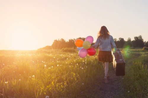 Pige, der går med balloner og en kuffert på en mark