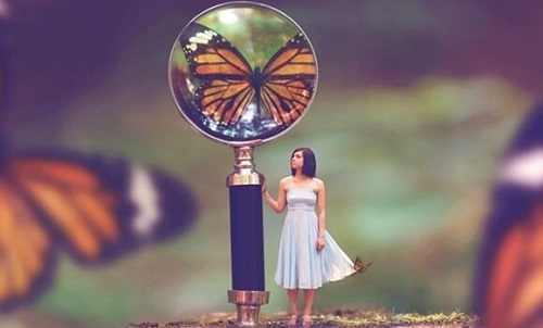 En lille pige ved siden af et forstørrelsesglas der viser en sommerfugl