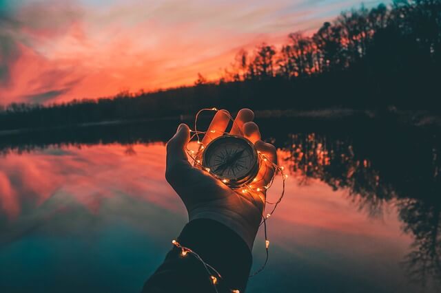 Person holder kompas i hånd foran solnedgang