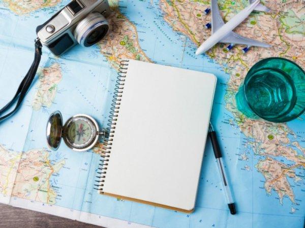 Blank notesbog ovenpå verdenskort med kamera, kompas, vandglas og fly