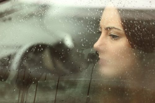 Kvinde kigger ud af vindue med regn på