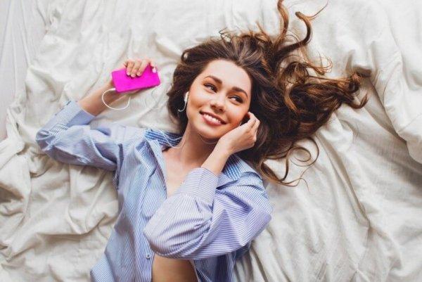 Smilende kvinde ligger i seng og lytter til musik
