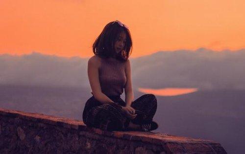 Kvinde sidder på mur foran landskab og solopgang