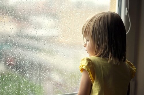 Lille pige ser ud på regn gennem vindue