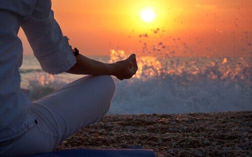 Person på strand mediterer ved solnedgang