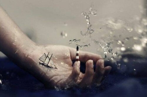 En hånd i vand, med en lille båd og et fyrtårn på fingeren