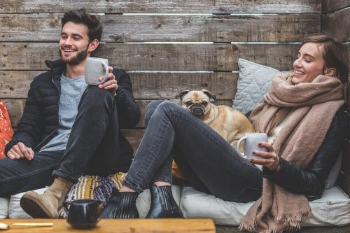 To venner griner og drikker kaffe udenfor med hund