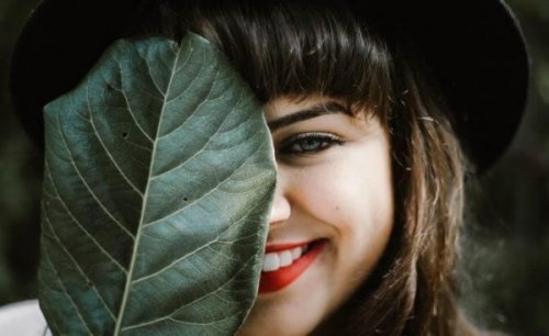 Smilende kvinde gemmer det ene øje bag stort blad