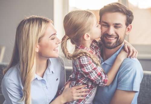 Pige kysser smilende far med mor ved siden af