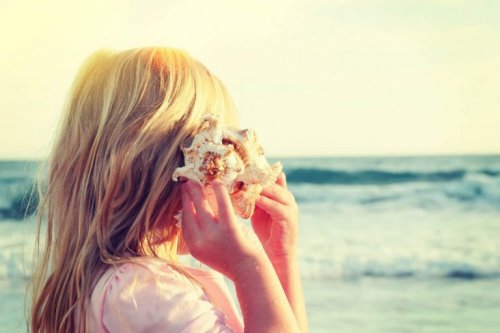 Selektiv opmærksomhed vist via en pige, der lytter til en konkylie på stranden