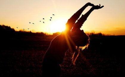 Kvinde med arme over hoved foran solnedgang