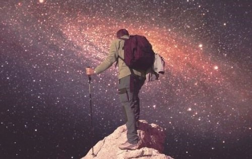 Mand på bjergtop foran universet illustrerer, at du skal tro på dig selv for at nå toppen