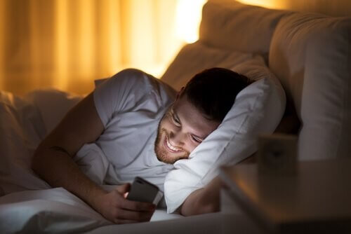 Mand kigger på sin telefon, mens han ligger i sengen