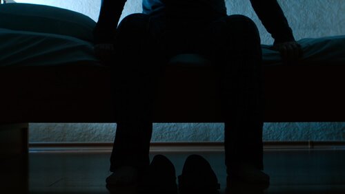 Mand sidder på sengen og lider af rastløse ben