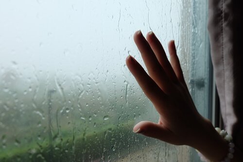 Kvinde lægger hånd på vindue med regn