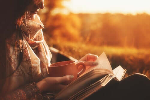 kvinde, der læser udenfor med en kop te