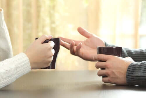 Personer taler sammen, hvilket kan ses på hænder, der holder om kaffekopper overfor hinanden