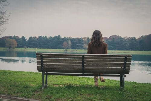 Kvinde sidder alene på bænk og ser på sø