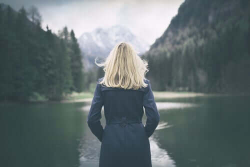 Kvinde ser på sø i skov og opfylder sit behov for alenetid