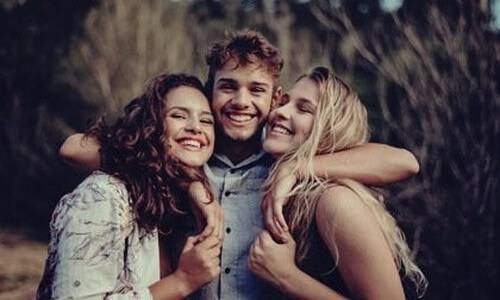 Smilende venner krammer på strand