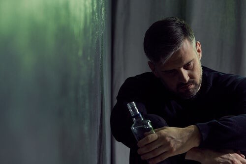 Mand ser nedtrykt ud, mens han sidder med en flaske alkohol