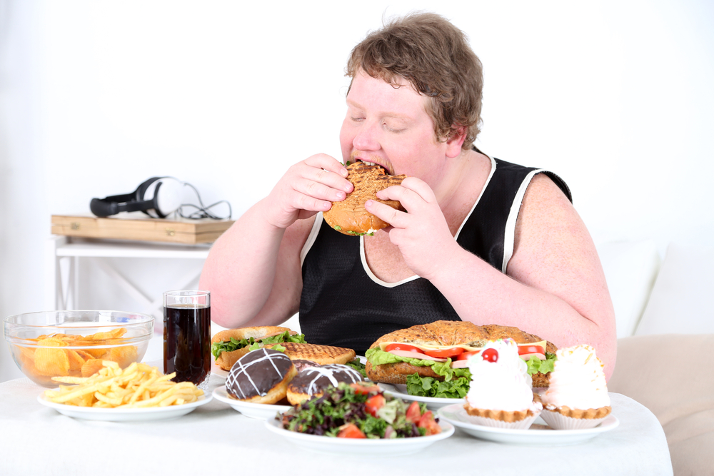 Person med alt for meget mad foran sig og burger i hånden