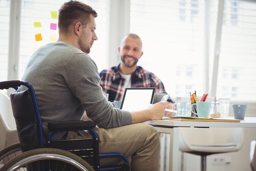 En mand i en kørestol sidder ved et bord og arbejder på sin bærbare computer og illustrerer inklusion af handicappede i samfundet