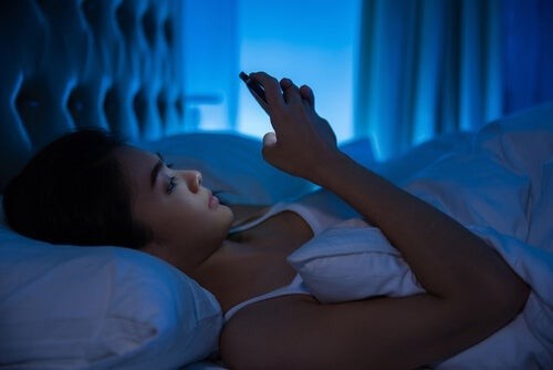 Der er en tæt forbindelse mellem elektroniske enheder og søvnændringer, hvilket illustreres af kvinde i seng med telefon