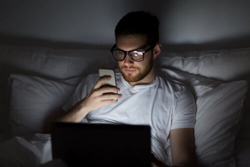 Mand bruger sin telefon og computer i sengen 