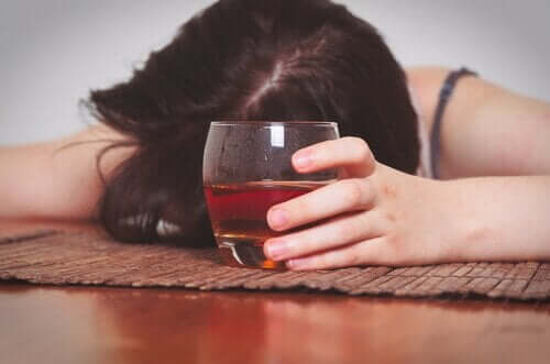 Kvinde med alkoreksi hviler hoved på bord og har et glas alkohol i hånden