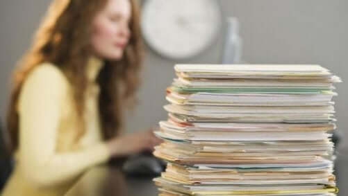 kvinde, der får adrenalinsus ved at udskyde ting, sidder med en masse papirer