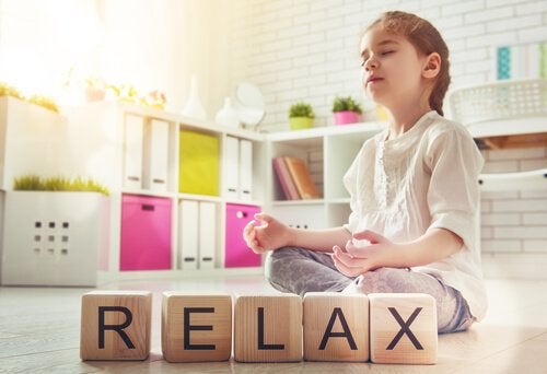 Pige mediterer ved siden af træklodser, der danner ordet "relax"