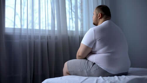 Overvægtig mand sidder på seng