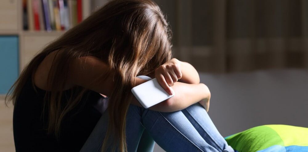 Pige med telefon i hånden gemmer sit ansigt som følge af online grooming