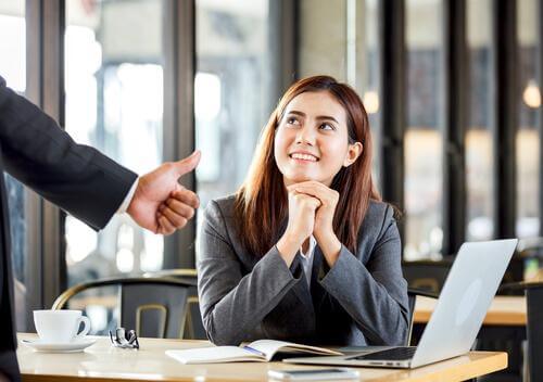 Smilende kvinde ved computer får tommel op af mand