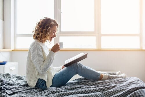 Kvinde læser en bog, mens hun sidder på sin seng