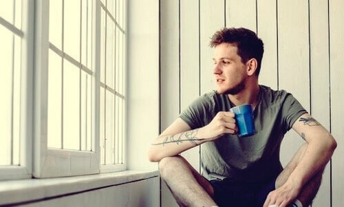 Mand drikker en kop kaffe, mens han kigger ud af vinduet 