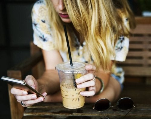 Ung kvinde, der får en iskaffe og bruger sin mobil