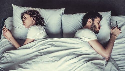 Par ligger i seng med hver deres telefon