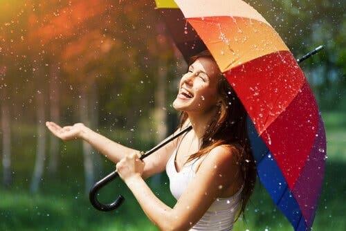 Glad kvinde i regnen under paraply