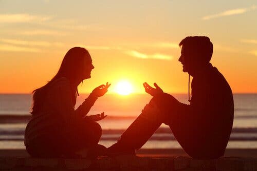 Mand og kvinde taler sammen på strand foran solnedgang