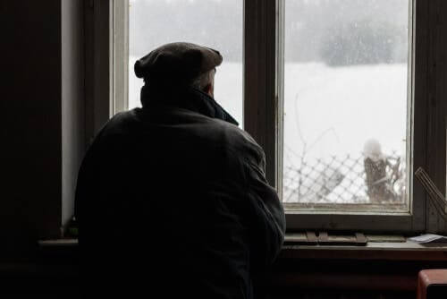 Gammel mand, der kigger ud af vindue