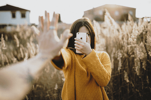 Personer rækker ud mod hinanden, men kvinde står med telefon i hånden som eksempel på, hvordan mobiltelefoner kan skade vores relationer