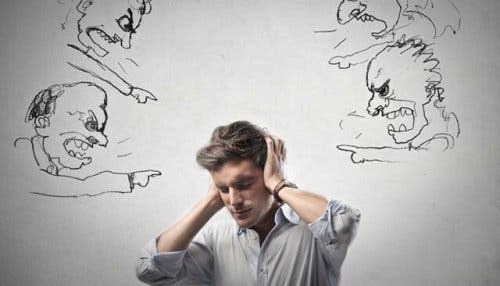 Mand holder sig for ørerne, mens tegninger råber kritik af ham fra alle sider