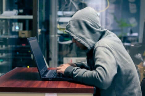 Mand med hættetrøje sidder ved computer og er i gang med phishing