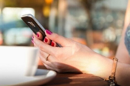 Kvinde sidder med sin smartphone på en café