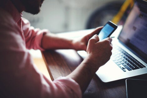 Mand, der sidder ved en computer med sin telefon